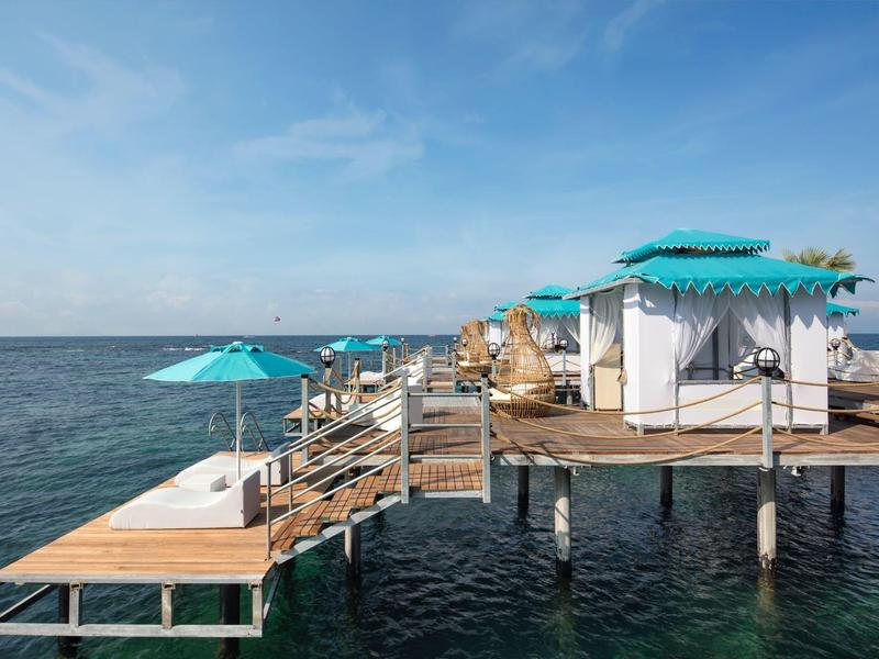Resort de playa de lujo con muelle de madera, tumbonas y sombrillas sobre el mar.