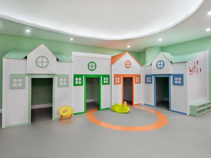Área de juegos para niños con estructuras de juego en forma de casas de colores en una habitación verde.
