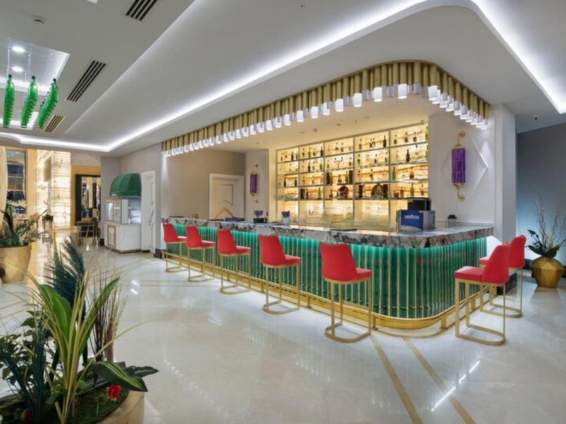 Área moderna de bar de hotel con barra verde, sillas rojas e iluminación elegante.