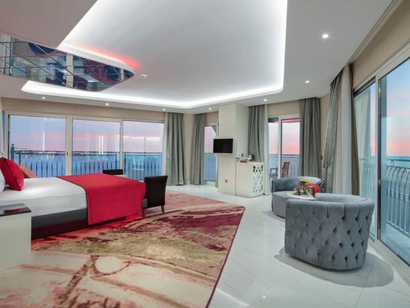Habitación de hotel moderna con cama grande, alfombra y ventanas panorámicas con vista al mar.