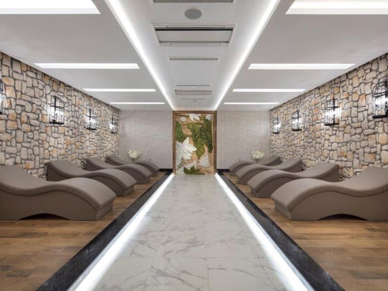 Área de bienestar moderna con paredes de piedra, tumbonas relajantes y iluminación cálida.