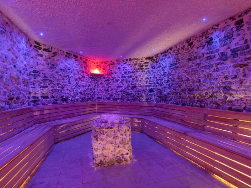Sauna con paredes de piedra, bancos de madera y iluminación ambiental colorida.