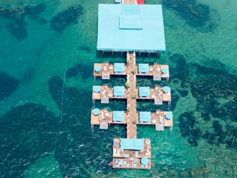 Vista aérea de bungalows sobre el agua en mar cristalino de color turquesa.