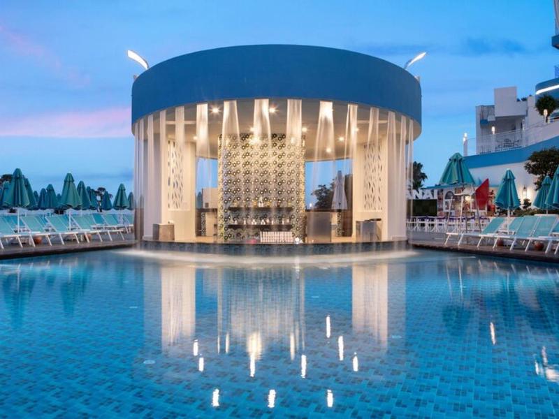 Piscina moderna redonda con bar, rodeada de tumbonas y suave iluminación nocturna.