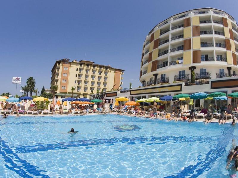 Großer Swimmingpool mit blauem Wasser vor runden und rechteckigen Hotels bei klarem Himmel.