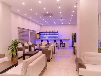 Moderner, heller Lounge-Bereich mit weißen Sofas, Holzmöbeln, Pflanzen und blau beleuchtetem Barbereich.