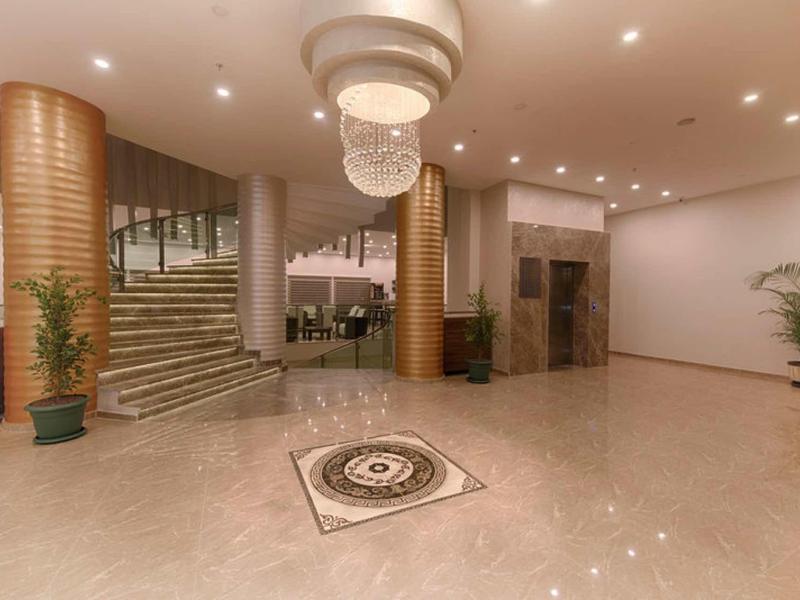 Spacious hotel lobby with marble floor, staircase, elevator, and chandelier.