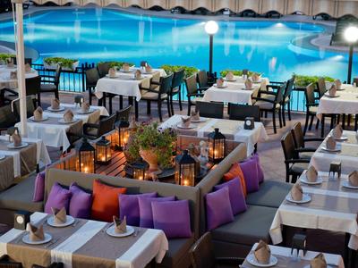 Elegant restaurant met witte tafels en paarse kussens, uitzicht op het zwembad bij schemering.