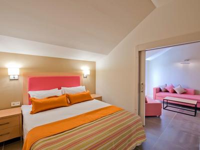 Gemütliches Schlafzimmer mit Doppelbett, orangefarbener Bettwäsche und angrenzendem Raum mit Sofa.