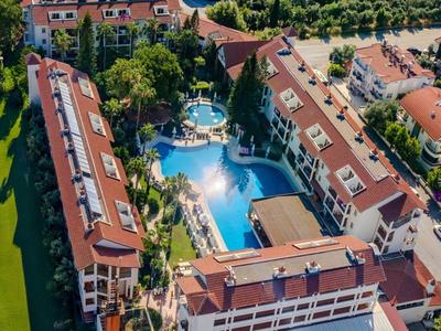 Veduta aerea di un hotel con grande piscina, circondato da tetti rossi e aree verdi.