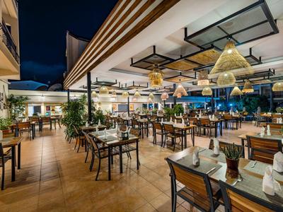 Modern openluchtrestaurant met stijlvolle houten tafels en warme verlichting 's nachts.