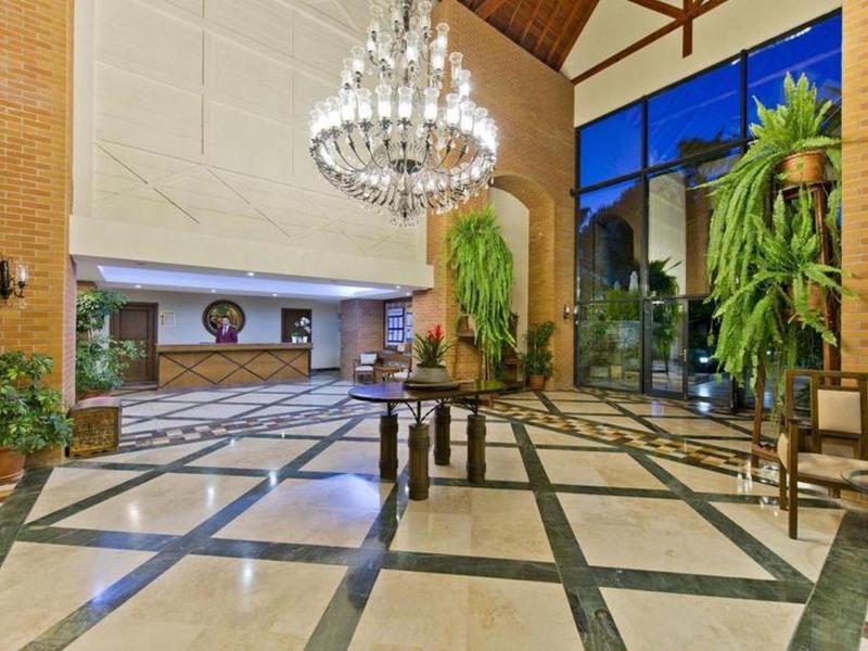 Große Hotel-Lobby mit Kronleuchter, Rezeption und viel Grün, Tageslicht durch Fenster