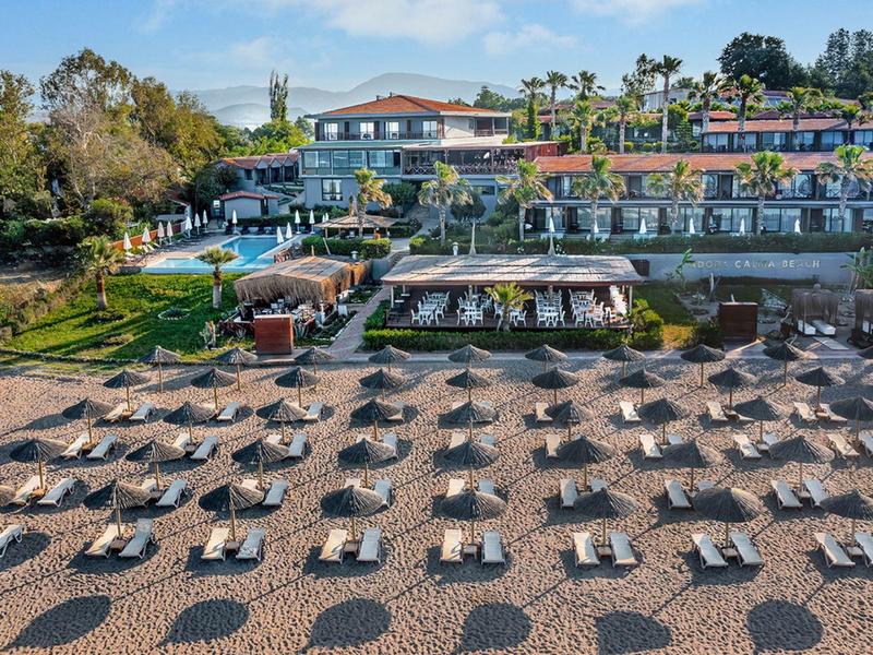 Hotel mit Terrassen und Reihen von Sonnenschirmen und Liegen auf einem Kieselstrand bei klarem Himmel.