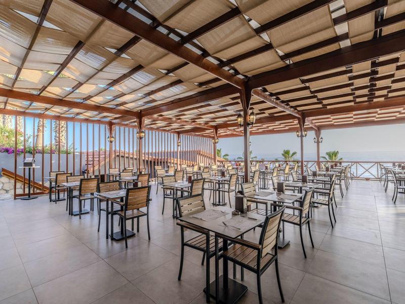 Großer, überdachter Außenbereich mit Tischen und Stühlen, frei und hell mit Blick ins Freie.