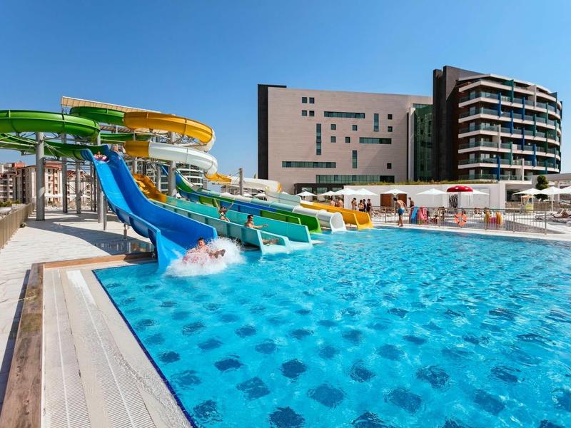 Glijbaan met water in buitenzwembad naast modern hotelgebouw bij heldere lucht.