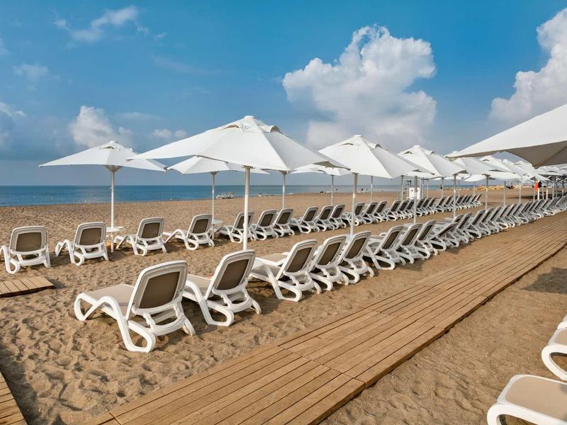 Reeks lege witte ligstoelen en parasols op zandstrand onder blauwe lucht.