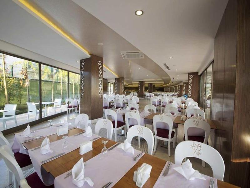 Modernes, helles Restaurant mit weißen Stühlen, Tischdecken und großen Fenstern zum Garten.