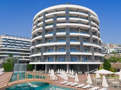 Rond hotelgebouw met meerdere balkons naast een zwembad en ligstoelen onder een blauwe lucht.
