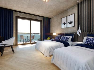 Modern hotelkamer met twee eenpersoonsbedden, bureau en balkon met zeezicht bij daglicht.