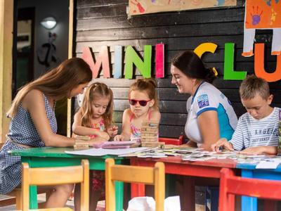 Fünf Kinder sitzen an buntem Tisch und malen auf Papier in kreativ gestaltetem Raum.