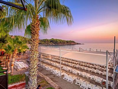 Prázdná pláž s mnoha lehátky a palmami při západu slunce.