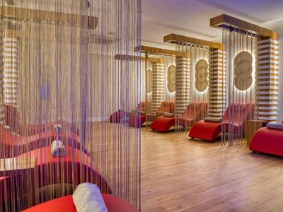 Ein moderner Wellnessraum mit roten Liegen, Holzboden und dekorativen Lichterrahmen an der Wand.