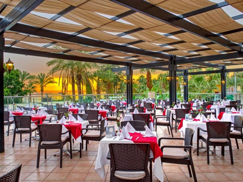 Offenes Restaurant mit gedeckten Tischen, Holzdach und Sonnenuntergang im Hintergrund.