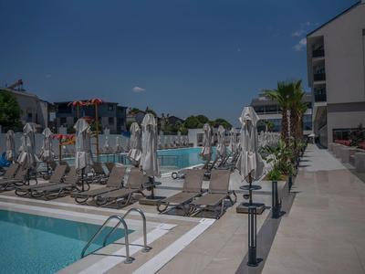Modern outdoor pool area with sun loungers and umbrellas beside a hotel building under a clear sky.