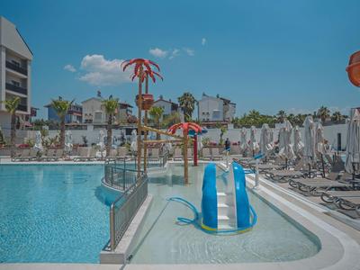 Pool area with water slides and sun loungers beside a hotel building.