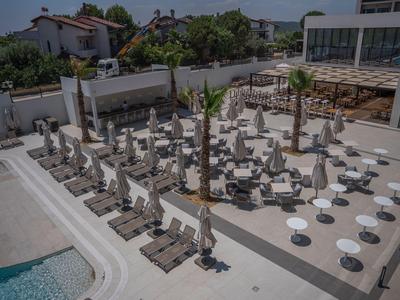 Modern hotel pool area with white umbrellas, sun loungers, and round tables on a light surface.