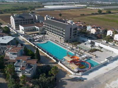 Large hotel with outdoor pool and water slides near the beach, surrounded by fields and houses.
