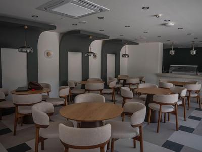 Modern empty hotel lounge with round wooden tables and upholstered chairs in neutral tones.