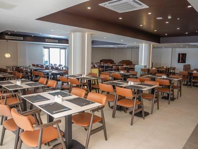 Large modern dining hall with many tables and orange chairs in a hotel.