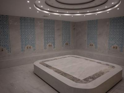 Elegant spa room with large heated stone basin and light blue mosaic walls.