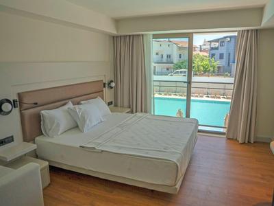 Bright hotel room with large bed, wooden floor, and pool view through floor-to-ceiling windows.
