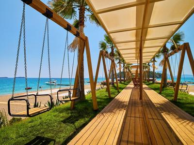 Covered wooden walkway with swing benches on the beach under palm trees on a clear day.