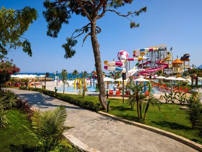 Wasserpark mit bunten Rutschen, Palmen und Gehweg unter blauem Himmel in sonniger Landschaft.