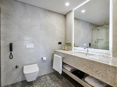 Modernes Badezimmer mit großer Spiegelwand, WC, Waschbecken auf grauer Steinablage und grauem Boden.