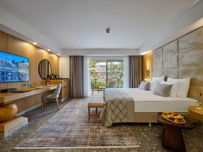 Helles, modernes Hotelzimmer mit großem Bett, Schreibtisch, Wand-TV und Zugang zu grünem Garten.