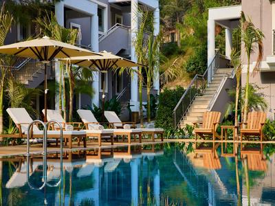 Pool area with lounge chairs, umbrellas, and adjacent hotel building in daylight