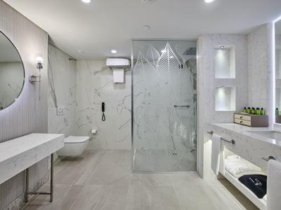 Helles Badezimmer mit Walk-In-Dusche, rundem Spiegel, Wand-WC und modernen weißen Fliesen.