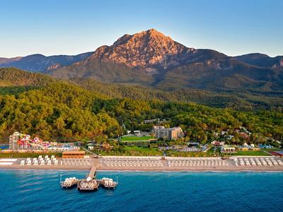 Strand mit Liegen, grüner Wald und Berge im Hintergrund unter blauem Himmel.