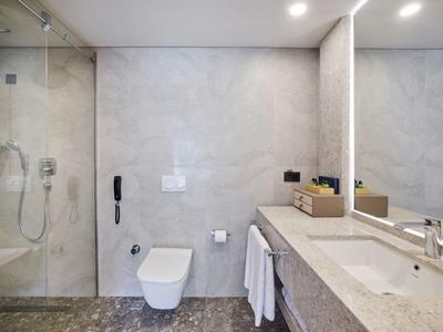 Moderne, helle Badezimmer mit grauen Fliesen, Dusche, Toilette, großem Spiegel und Waschtisch.