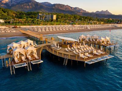 Large wooden platform with sun loungers on the sea, backed by forested mountains and beach.