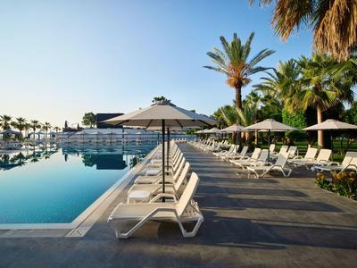 Leżaki ustawione wzdłuż basenu na świeżym powietrzu pod parasolami.