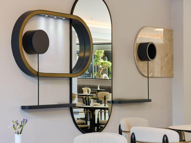 Moderne weiße Stühle und schwarze Tische in einem hellen Raum mit ovalen Spiegeln an der Wand.