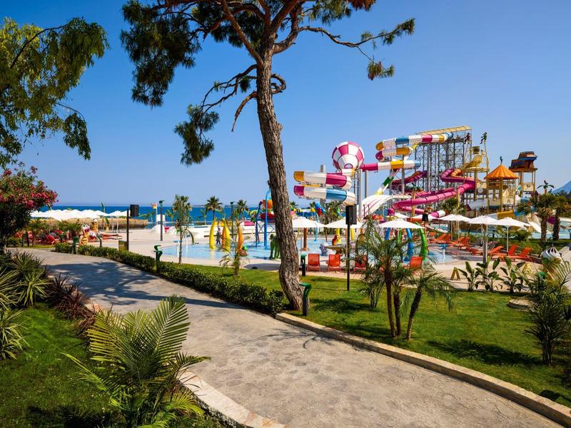 Wasserpark mit bunten Rutschen, Palmen und Gehweg unter blauem Himmel in sonniger Landschaft.