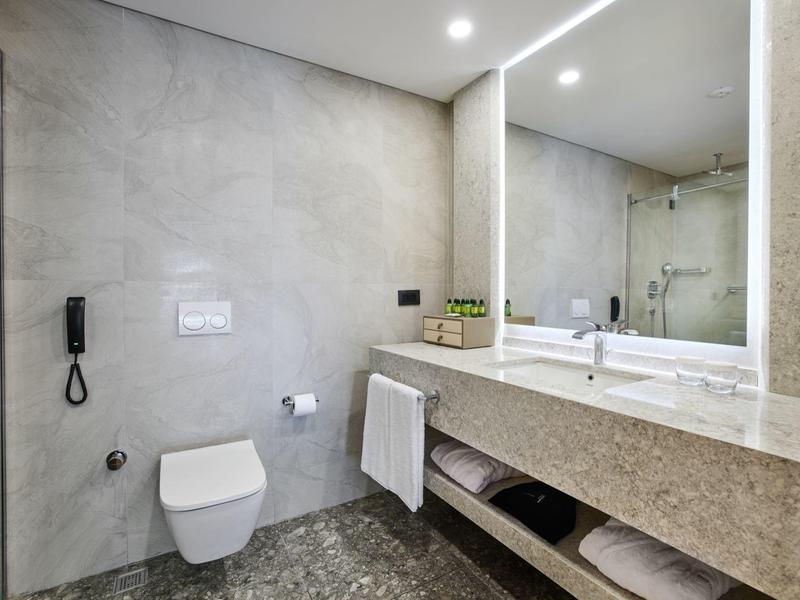 Modernes Badezimmer mit großer Spiegelwand, WC, Waschbecken auf grauer Steinablage und grauem Boden.