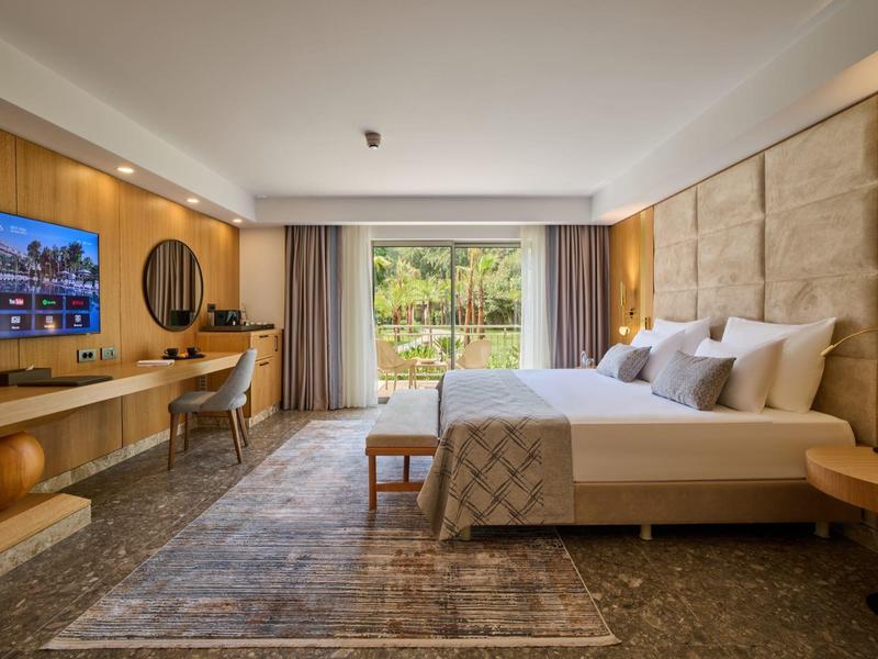 Modernes Hotelzimmer mit großem Doppelbett, TV, Schreibtisch und großer Fensterfront zum Garten.