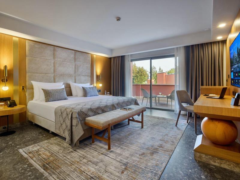 Modernes Hotelzimmer mit Doppelbett, Balkon, warmen Holzakzenten und gemütlicher Beleuchtung.